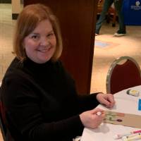 A woman sitting at a table decorating lunch bags for Kids' Food Basket